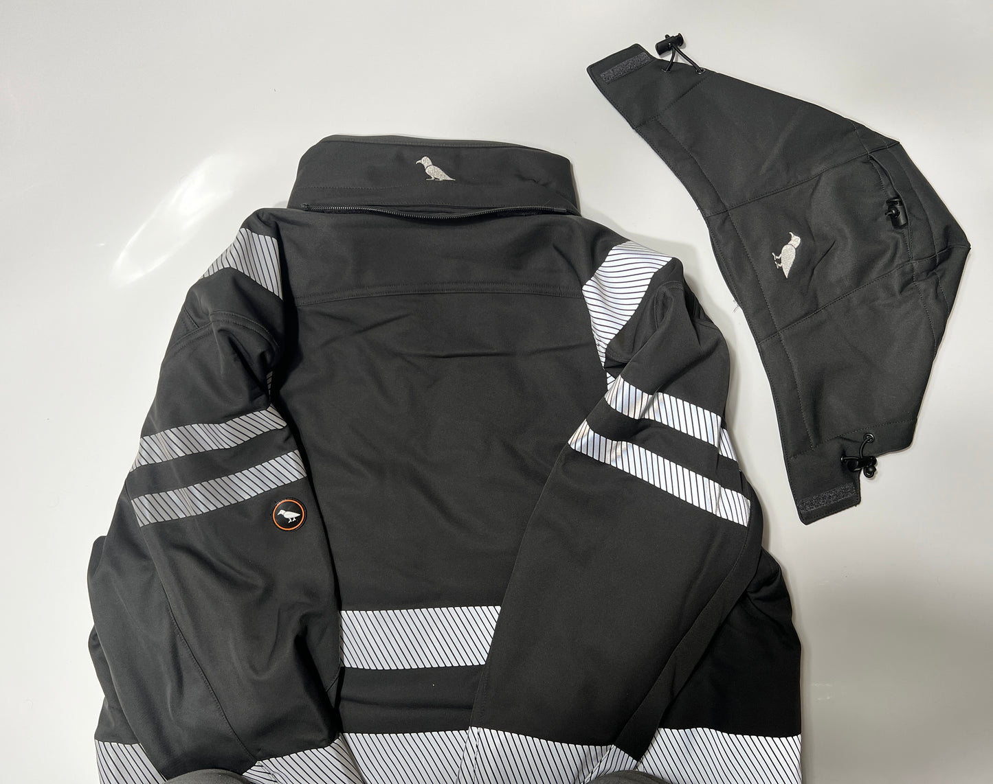Eine schwarze Kapuze liegt neben der schwarzen Softshelljacke mit Reflektoren