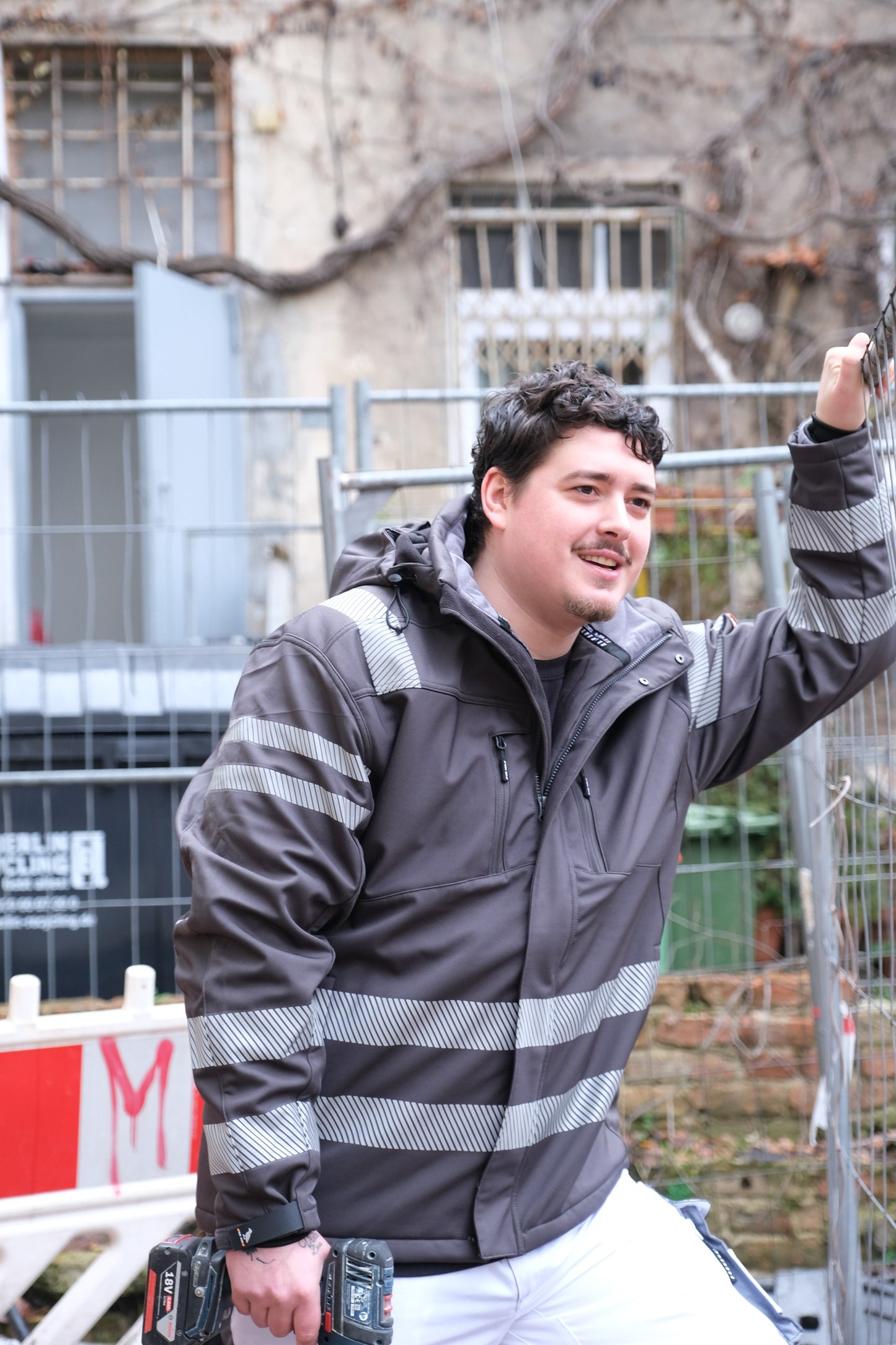 Ein Mann mit einer schwarzen Jacke mit Reflektoren auf einer Baustelle