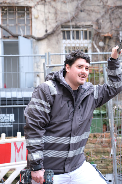 Ein Mann mit einer schwarzen Jacke mit Reflektoren auf einer Baustelle