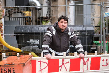 Ein Mann mit einer schwarzen Jacke mit Reflektoren auf einer Baustelle